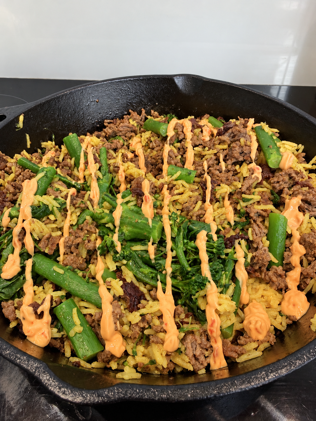 A pan of rice, green vegetables and minced beef finished with lines of orange samurai sauce.